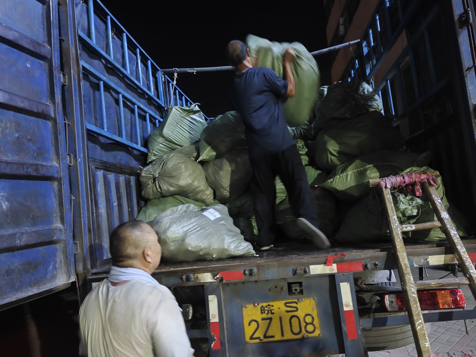 A China-side operations worker lifting a parcel sack into a truck during a night loading run
